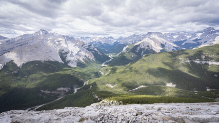 View on beautiful alpine valley from mountain summit with dramatic cloudy sky, shot during summer day at Nihahi Ridge, Kananaskis, Alberta, Canada