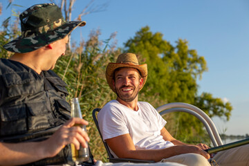 Smiling man with his friend sitting and enjoying at the lake with a beer bottle in her hand.