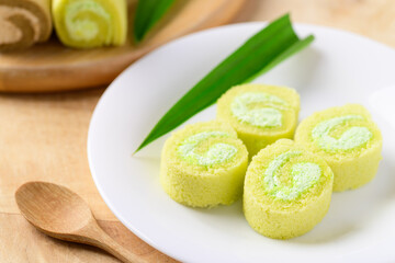 Sliced pandan roll cake with pandan leaf on white dish and spoon on wooden table