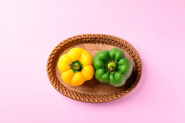 Yellow and green bell peppers in woven rattan basket on pink background, Top view