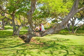 Naklejka na ściany i meble Teen girl resting on large tree branch at tropical park