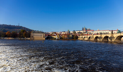 Obraz premium Autumn colorful Prague Lesser Town with gothic Castle and Charles Bridge above River Vltava in the sunny Day, Czech Republic