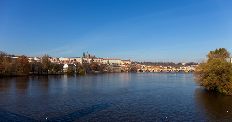 Fototapeta premium Autumn colorful Prague Lesser Town with gothic Castle and Charles Bridge above River Vltava in the sunny Day, Czech Republic