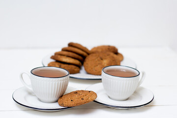 Two cups of tea and oatmeal cookies. Breakfast. Tea drinking. White wooden background.