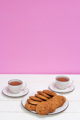 Two cups of tea and oatmeal cookies on a white wooden table and pink background. Breakfast.