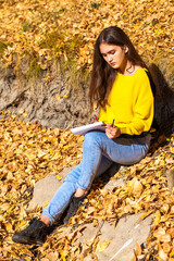 Brunette girl draws with a pencil in the sketchbook in the autumn park