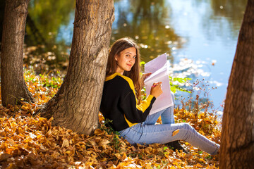 Brunette girl draws with a pencil in the sketchbook in the autumn park