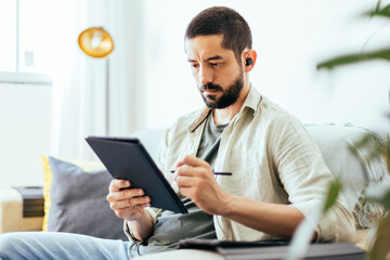 Fototapeta na wymiar Young bearded man working from home. Man on sofa at home using digital tablet