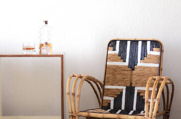 Plano cerrado de un sillón de mimbre vacío junto a una botella y un vaso con whisky escocés en...