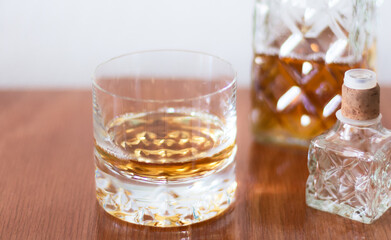 Primer plano de un vaso de cristal con whisky escocés junto a una botella lujosa y con estilo en un ambiente blanco e iluminado con luz natural
