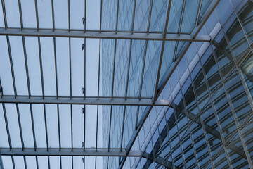 Low angle view of skylight with rectangular grid pattern over atrium which connect to curvature glass building's facade.  
