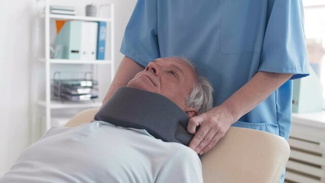 Medium shot of unrecognizable female doctor putting bandage on neck of elderly male patient lying on exam couch in medical office