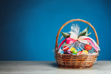 Fototapeta na wymiar Easter gift basket with multicolor eggs, blue background