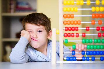Caucasian toddler boy feeling bored and tired while playing with abacus at kindergarten