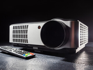 A multimedia projector stands on a wooden table. Video projector with remote control. Equipment for...