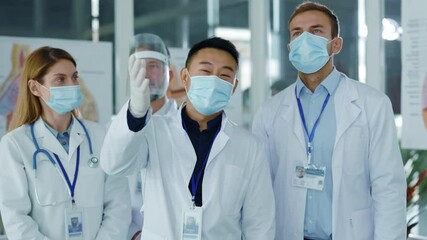 Diverse young doctors team communicating in medical office wearing masks agree to nee vaccination applauding successful meeting. Professional staff. Quarantine. Coronavirus. - Powered by Adobe