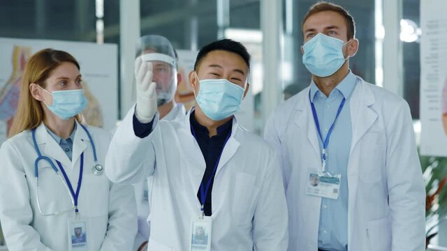 Diverse young doctors team communicating in medical office wearing masks agree to nee vaccination applauding successful meeting. Professional staff. Quarantine. Coronavirus.