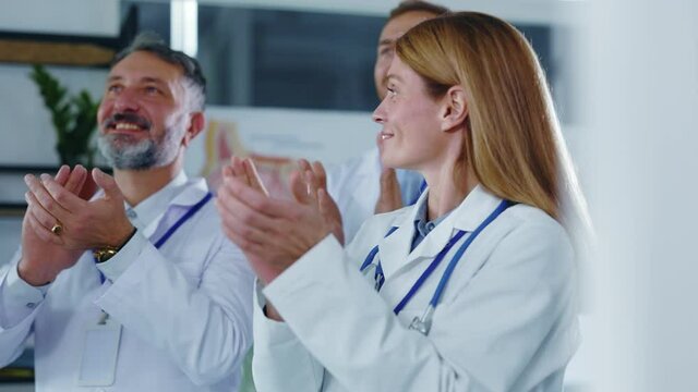 Multi-race professional medical staff with female boss applauding ending quarantine coronavirus finished congratulating doctors watching TV in hospital office.