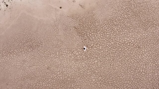 Lone Man Walking Across Dry Desert Land During Drought Season - aerial top-down