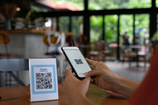 Woman is using a mobile phone to scan a QR coach to pay for food and drinks instead of cash in a coffee shop. QR code payment and cash technology concept.