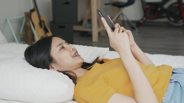 Smiling Asian woman lying on bed and using smartphone online social.
