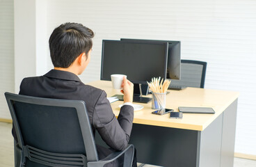 Asian businessman wearing a black suit sitting at office desk having a coffee break and Thinking about business plan,Relaxed,rear view