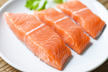 Raw salmon filet with herbs and spices on white plate and wooden background. /