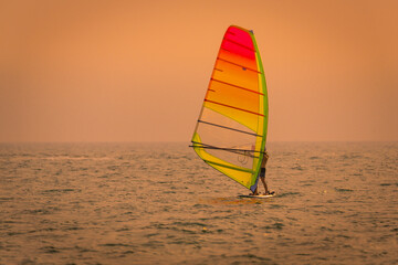 Silhouette sportsman is windsurfing at sunset time on wind of wave 