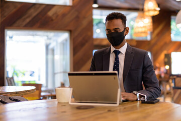 Businessman using laptop while wearing protective facial mask in coffee shop