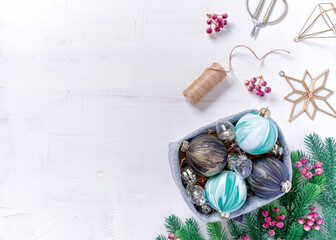 Christmas composition. Paper Christmas decorations are in a felt basket. Spruce branches and berries are nearby. Painted white background. Flat lay, top view.