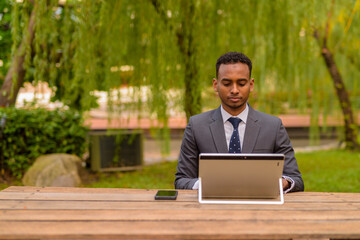 African businessman sitting outdoors using laptop computer
