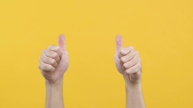 Close up of Man’s hand gestures. Approval like. Man showing thumb up isolated on yellow copy-space background.