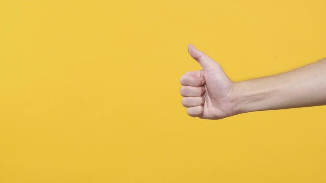 Close up of man&rsquo;s hand pointing to the left side showing thumb up sign isolated on a yellow background with copy space for place a text, message for advertisement, and promotional
