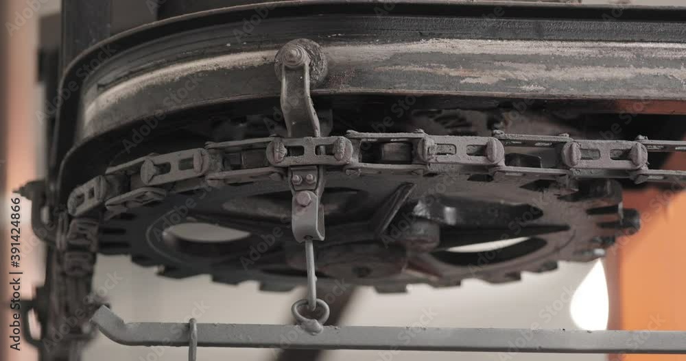 Poster mechanical gear with metal chain rotating slowly in a factory - close up