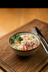 Traditional russian new year salad with boiled rice, canned corn and crab meat in a small bowl on a rustic table
