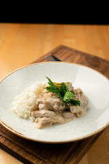 Close up of creamy beef stroganoff with thin beef slices and boiled rice, decorated with pickles cucumber, restaurant serving