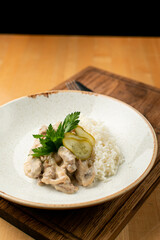 Close up of creamy beef stroganoff with thin beef slices and boiled rice, decorated with pickles cucumber, restaurant serving