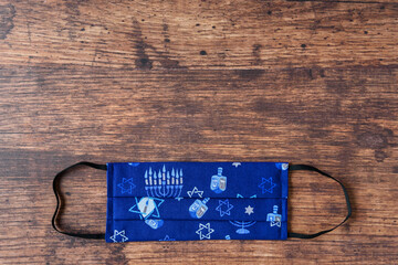 Hand made fabric masks on a wood background, celebrate Hanukkah with Jewish symbols on a blue mask
