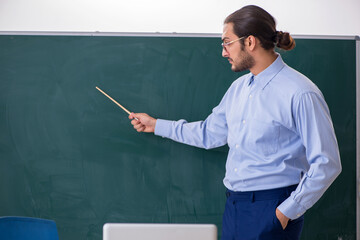 Young male teacher in the classroom in front of green board