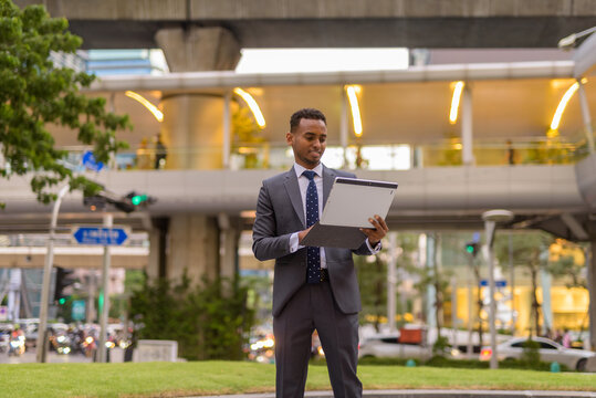 African businessman outdoors using laptop computer while standing