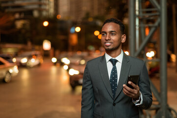 African businessman using mobile phone app waiting for taxi at night