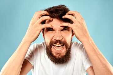 Bearded man in white T-shirt emotions gestures with hands displeased facial expression blue background