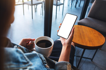 Mockup image of a woman holding mobile phone with blank white desktop screen while drinking coffee