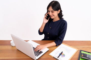 An attractive and cheerful young business woman working on a laptop and smiling as she sits on the phone. At her desk modern office