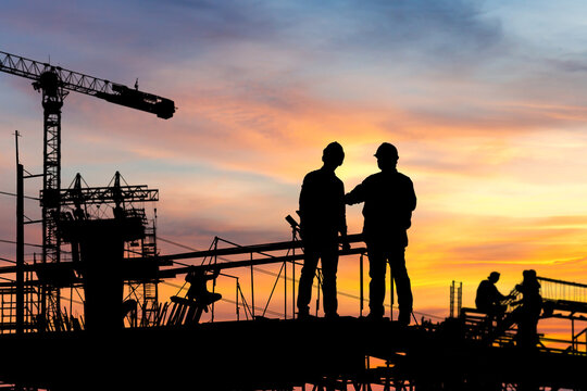 Silhouette of Engineer and worker checking project at building site background, construction site at sunset in evening time.