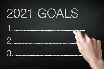 Hand holding a chalk and writing 2021 goals