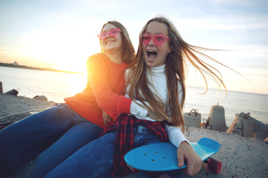 Two female friends playing with skateboard skateboard in the park. Girls with a skateboard. Laughter and fun. High quality photo.