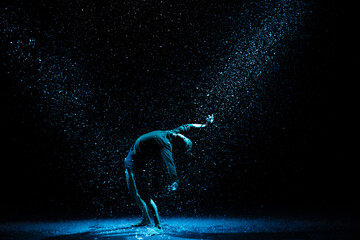 Ballet dancer against the background of falling snow and studio light. A man posing on a black background.