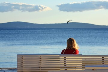 woman sitting on bench looking over the sea with seagull in background/ Relaxation/Meditation time concept.