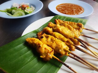 grilled Thai style Chicken satay on banana leaf decorated plate along with side dishes